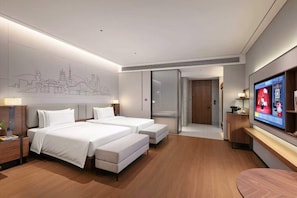Ein Hotelzimmer mit zwei Betten, einem Fernseher, einem Stadtbild als Kunstwerk und einer SchiebetĂŒr zu einem Badezimmer.