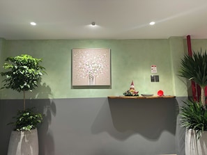 A reception area with a green wall, a painting of flowers, a reception desk, and potted plants. - Phuc Loc Premier (Ben Thanh)