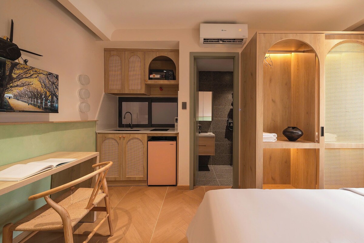 A compact hotel room with a bed, a desk, a kitchenette, and a bathroom.
