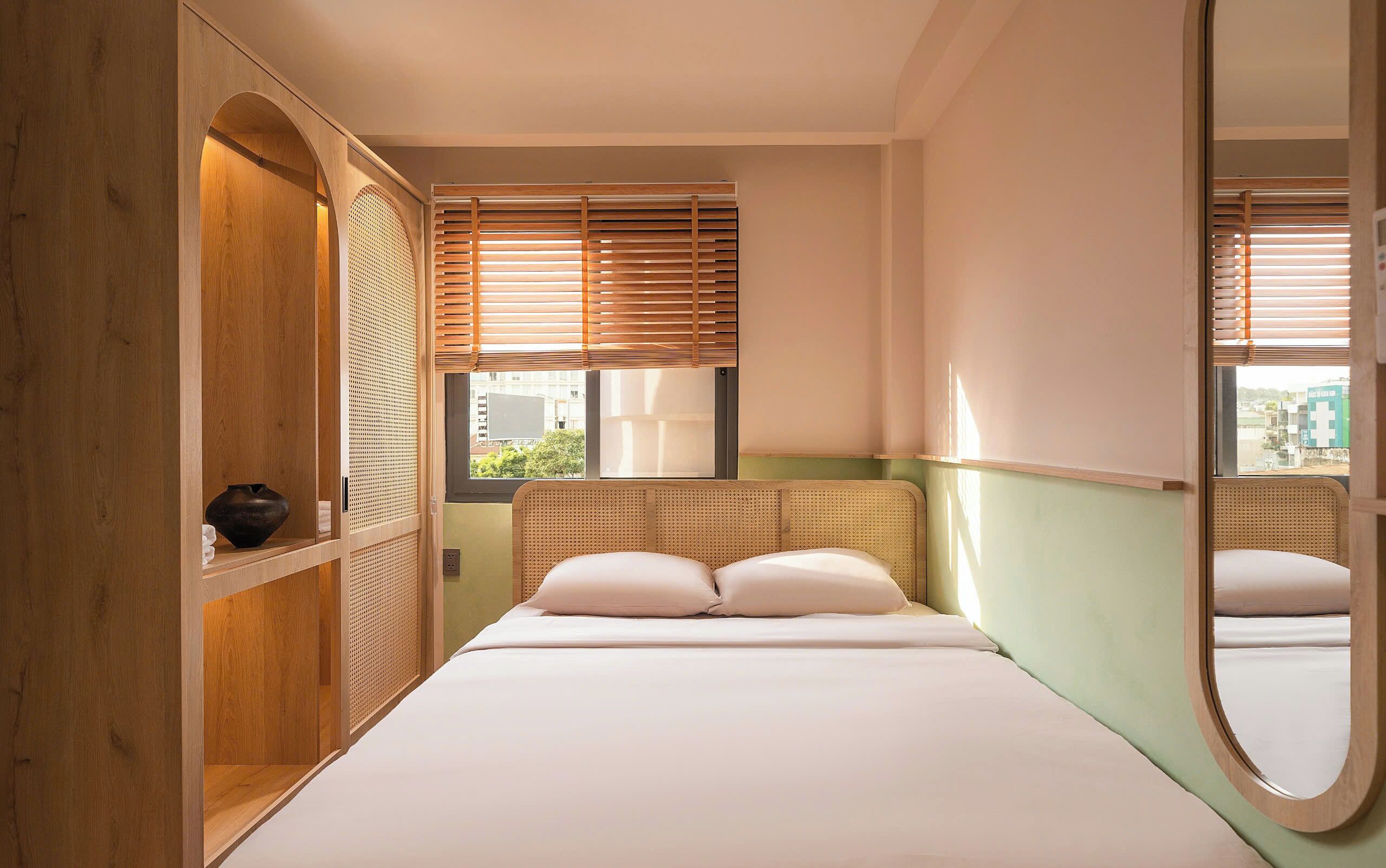 A bedroom with a bed, wooden wardrobe, and a window with blinds.