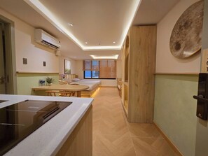 Una cocina moderna con estufa integrada, un comedor con mesa de madera y un dormitorio con cama y persianas.
