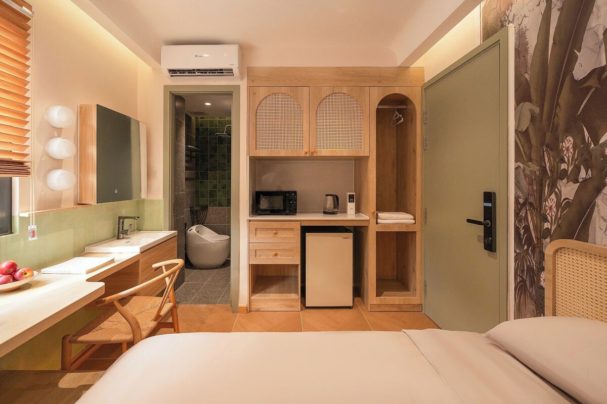 A compact hotel room with a desk, a chair, a bed, a wardrobe, and a shower area.
