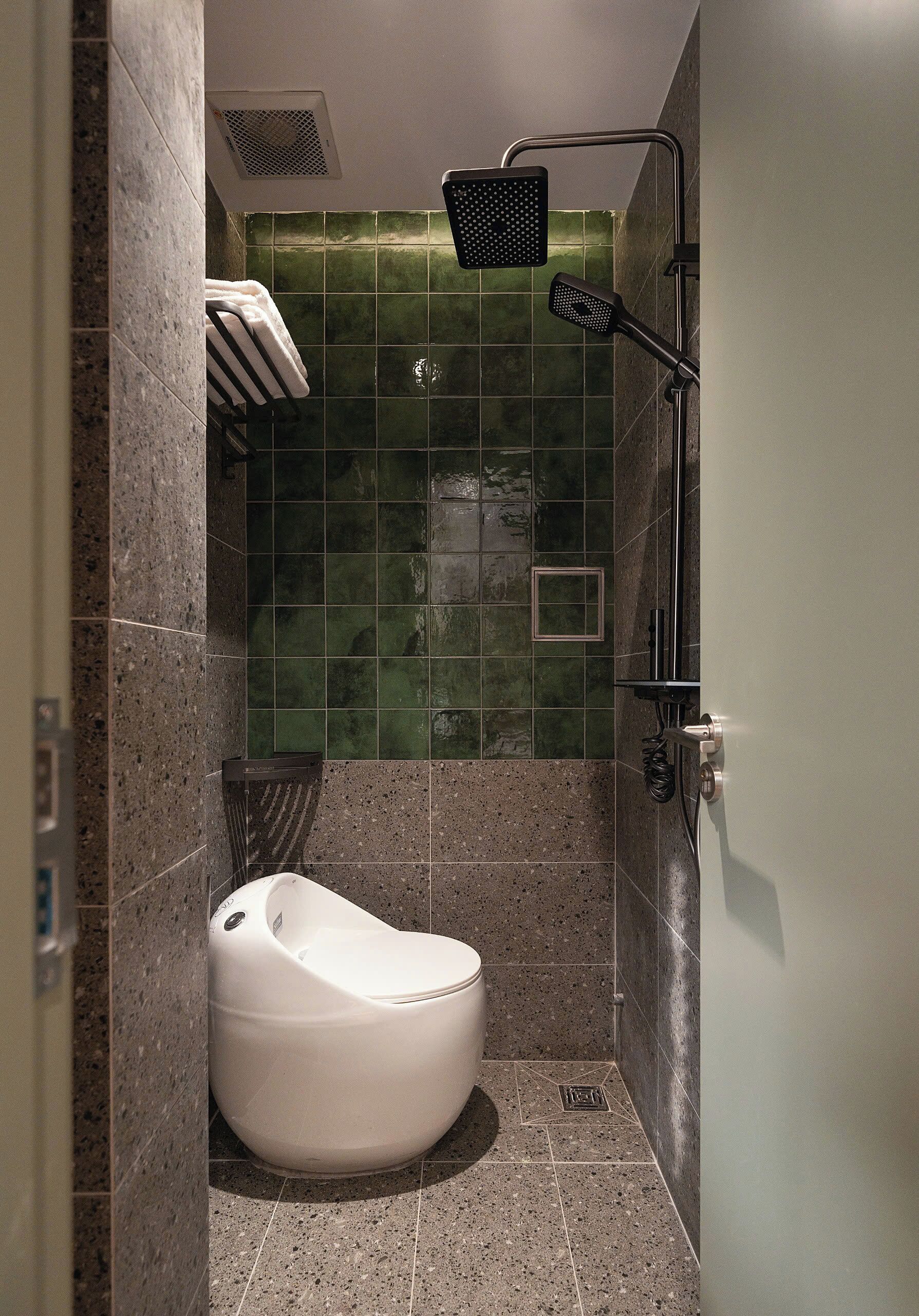 A modern bathroom with a white toilet, a shower with a handheld showerhead, and green tiled walls.