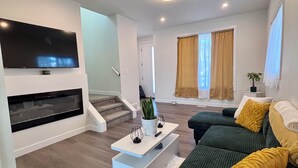 Ein modernes Wohnzimmer mit Flachbildfernseher, Couchtisch, Sofagarnitur und einer Treppe, die eine weitere Ebene hinaufführt.