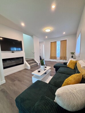 Ein modernes Wohnzimmer mit Flachbildfernseher, Couchtisch, Sofagarnitur und einer Treppe, die eine weitere Ebene hinaufführt.