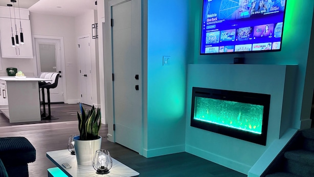 Ein modernes Wohnzimmer mit einem an der Wand befestigten Flachbildfernseher, einem integrierten Kamin und einem Essbereich, im Hintergrund befindet sich eine Küche.