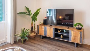 Ein Wohnzimmer mit einem TV-Schrank aus Holz, einer großen Kübelpflanze, einer kleinen Bonsai und einem dekorativen Vogel.