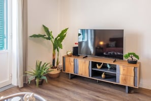 Ein Wohnzimmer mit einem TV-Schrank aus Holz, einer großen Kübelpflanze, einer kleinen Bonsai und einem dekorativen Vogel.