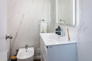 Un bagno con lavandino bianco, bidet, specchio e articoli da toilette sul mobile.