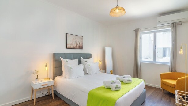 Ein Hotelzimmer mit Bett, Nachttischen, einem Sessel, einem Fenster und einer Pendelleuchte.