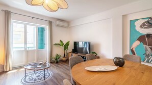 Ein modernes Wohnzimmer mit einem runden Holzesstisch, einem Fernseher und einem großen Fenster mit Jalousien.