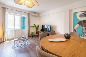 Ein modernes Wohnzimmer mit einem runden Holzesstisch, einem Fernseher und einem großen Fenster mit Jalousien.