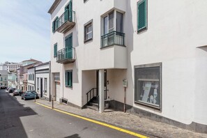 Una strada con un edificio bianco, dotato di balconi, una scala e un'auto parcheggiata.