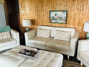 Un salón con un sofá, dos sillones, una mesa de centro y una pared de madera con un cuadro enmarcado.