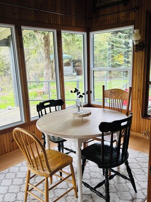 Una habitación con paneles de madera, una mesa redonda y sillas, ventanas grandes y vistas al exterior.