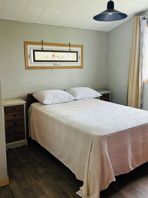 Une chambre à coucher comprenant un lit, une commode, une table de chevet, une fenêtre avec des rideaux et un luminaire au plafond.