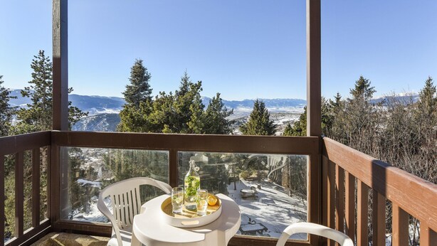 Ein Balkon mit Tisch und Stühlen, der auf eine verschneite Landschaft mit Bäumen und Bergen blickt.