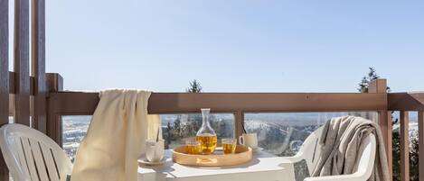 A balcony with two white chairs, a table with a tray of drinks, and a view of a snowy landscape.