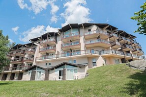 Un hotel de diverses plantes amb balcons, una pendent herbosa i un cel serè.