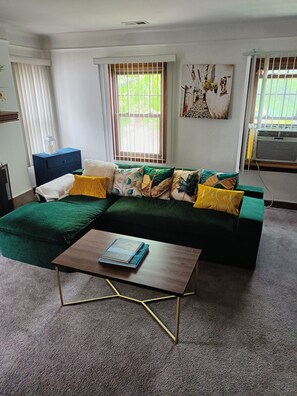 Una sala de estar con un sofá verde, una mesa de centro y un ventanal con persianas.