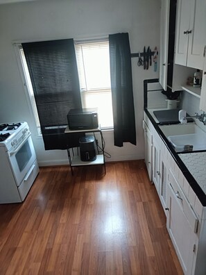A kitchen with a stove, oven, and a coffee maker on a cart, with a window and curtains.