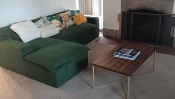 A living room with a green sofa, a wooden coffee table, and a fireplace.