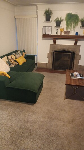Ein Wohnzimmer mit einem grünen Sofa, einem Holztisch, einem Kamin und einem Bücherregal mit Pflanzen.