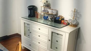 A white cabinet with drawers, a coffee maker, and a coffee bar sign on the wall.