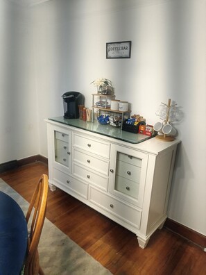 A white cabinet with drawers, a coffee maker, and a coffee bar sign on the wall.