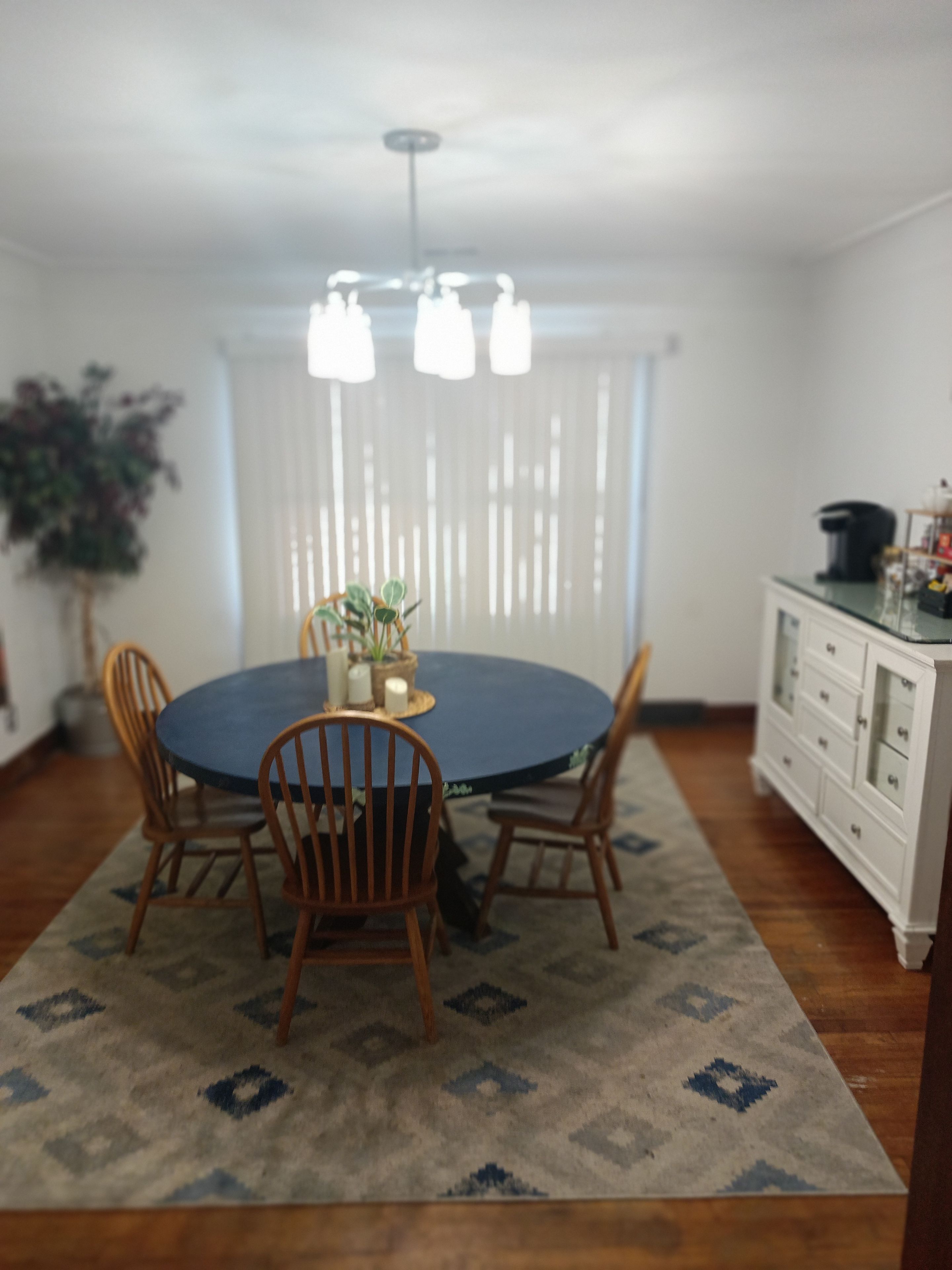 A dining area with a round table, four chairs, a chandelier, and a white cabinet with drawers.