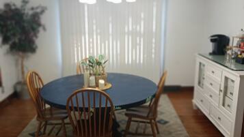 A dining area with a round table, four chairs, a chandelier, and a white cabinet with drawers.
