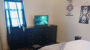 A bedroom with a bed, a dresser, a television on the dresser, a window with curtains, and a patterned rug. - Charming Upper Flat 10 mins from Downtown Det-10 mins from Nautical Mile (Detroit)