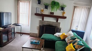 A living room with a green sofa, a television, a coffee table, and a fireplace. - Charming Upper Flat 10 mins from Downtown Det-10 mins from Nautical Mile (Detroit)