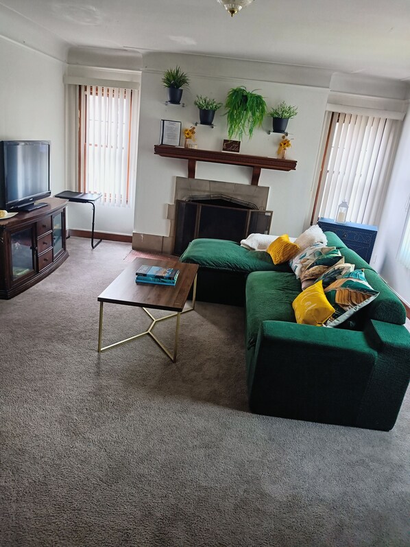 Una sala de estar con un sofá verde, televisor, mesa de centro y chimenea.