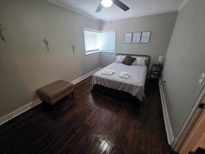 Ein Schlafzimmer mit einem Bett, einer Sitzbank, einem Deckenventilator, einem Fenster mit Jalousien und Wanddekorationen.