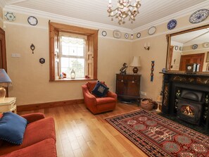A living room with a fireplace, wooden flooring, a red armchair, a patterned rug, and a large mirror. - WHITE HEATHER COTTAGE, family friendly in Killaloe, County Clare (Killalou)