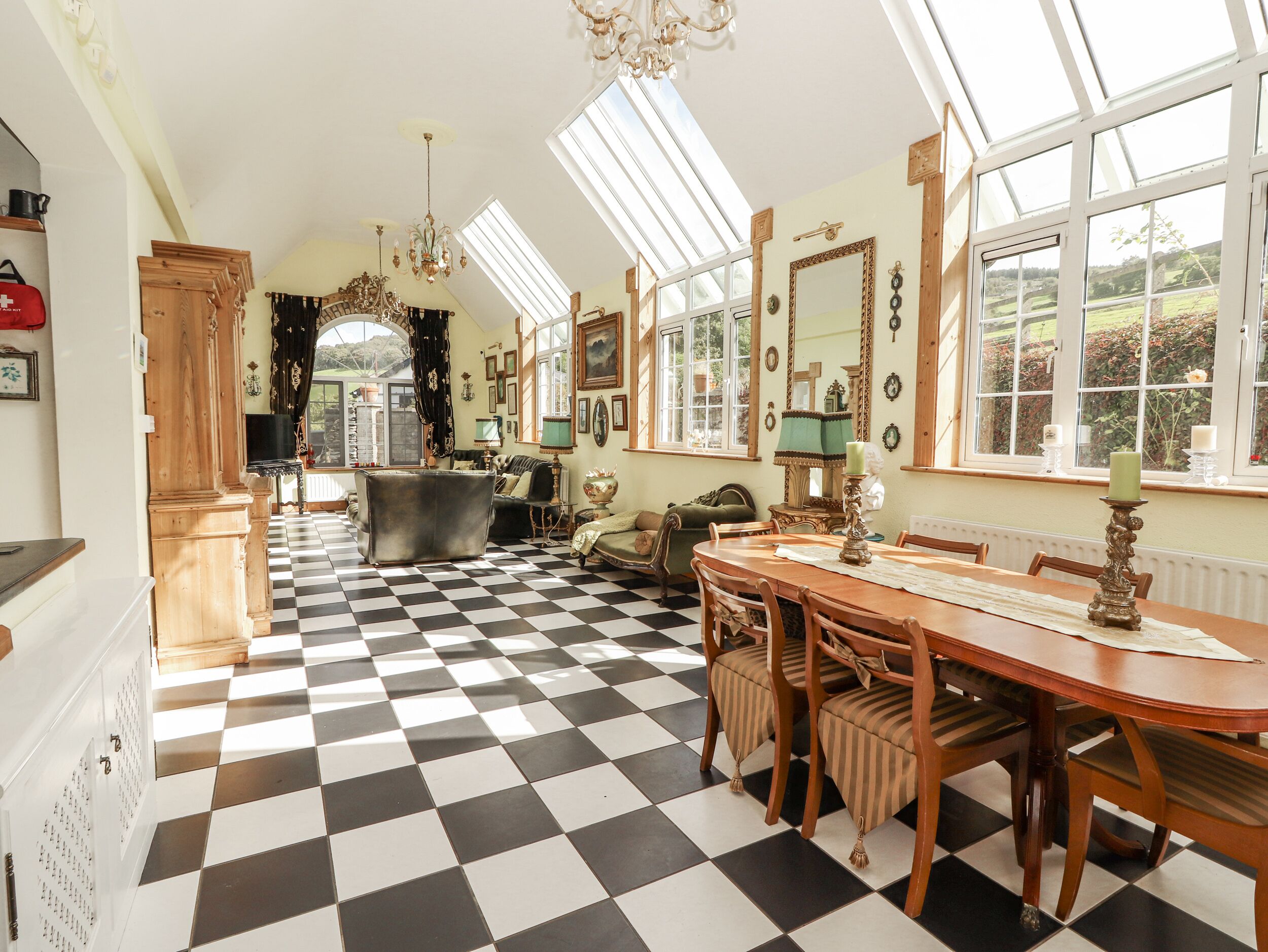 A room with a checkered floor, a dining table with chairs, a chandelier, and large windows.