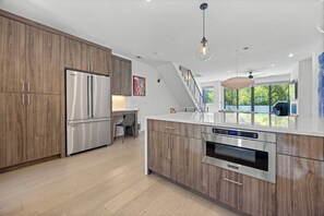 A modern kitchen with stainless steel appliances, wooden cabinetry, and a dining area with a view.