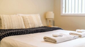 Un lit bien fait, recouvert d’une couette blanche et d’une couverture à rayures foncées. Deux serviettes blanches pliées sont posées sur le lit.