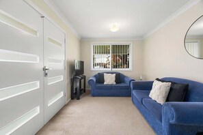 Ein Zimmer mit Fernseher, zwei Sofas, einem kleinen Tisch und einem Fenster mit Gitterstäben.