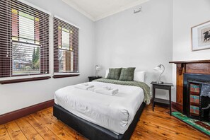 Ein Schlafzimmer mit einem Bett, zwei Nachttischen, einem Schreibtisch, einem Kamin und einem Fenster mit Jalousien.
