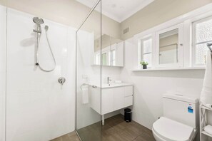Ein modernes Badezimmer mit Duschkabine aus Glas, einem weißen Waschbecken mit Spiegel darüber und einer Toilette.