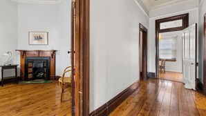 A hallway with wooden flooring, a fireplace, a framed picture on the wall, and a door leading to another room. - Dalton Bungalow - Heritage Character (Orange)
