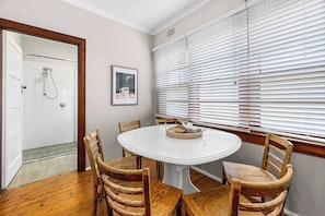 A room with a round table, four wooden chairs, a framed picture on the wall, and a window with blinds. - Dalton Bungalow - Heritage Character (Orange)