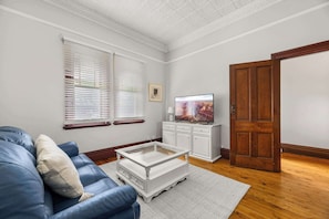 A living room with a blue sofa, white coffee table, wooden floor, white walls, and a wooden door. - Dalton Bungalow - Heritage Character (Orange)