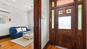 A room with a wooden floor, a blue leather sofa, a white coffee table, and a wooden door with stained glass panels. - Dalton Bungalow - Heritage Character (Orange)