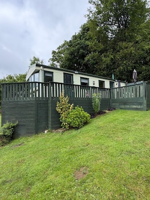A mobile home with a fenced yard, a small garden, and a tree in the background. - Family & Dog Friendly 2-Bed Caravan, Sleeps 6 (Newton Stewart)