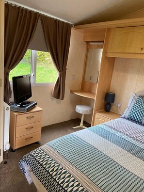 A bedroom with a bed, a desk, a chair, a television, and a window with curtains.