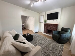 Ein Wohnzimmer mit einer Couch, Hocker und Kamin.