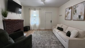 Ein Wohnzimmer mit Flachbildfernseher, Kamin aus Ziegeln, einer Couch, einem gemusterten Teppich und abstrakten Wandbildern.